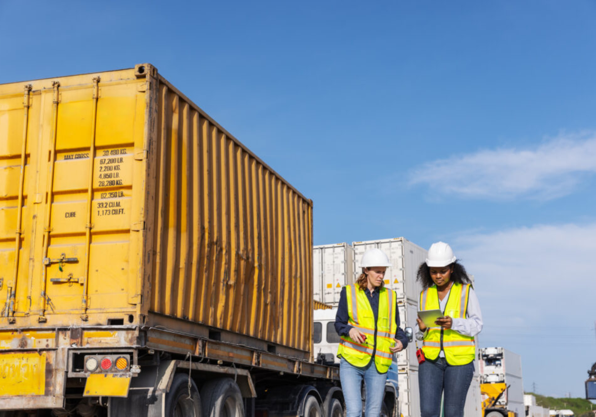 Two female workers wearing safety vests and hard hats standing on-site