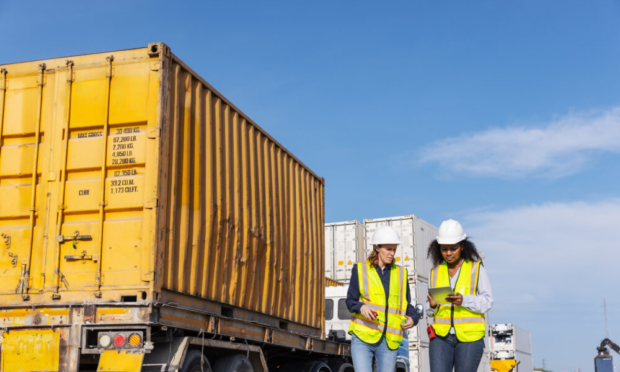 Two female workers wearing safety vests and hard hats standing on-site